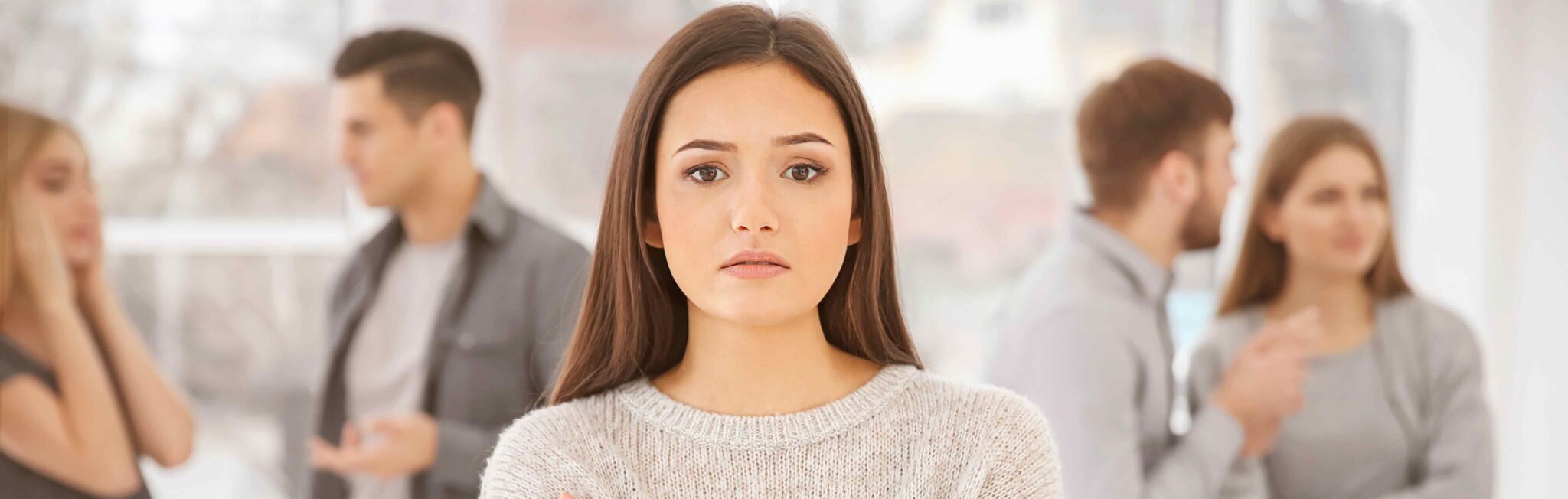 Image of a woman in the foreground with a confused and worried, detached expression while other people interact in a blurred background, suggesting her difficulty in connecting socially.